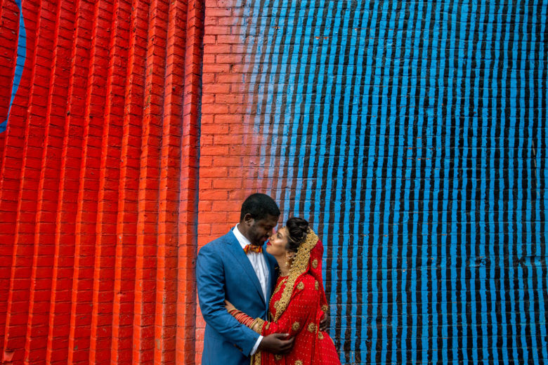 couple wearing blue and red embracing in front of a blue and red graffitied wall