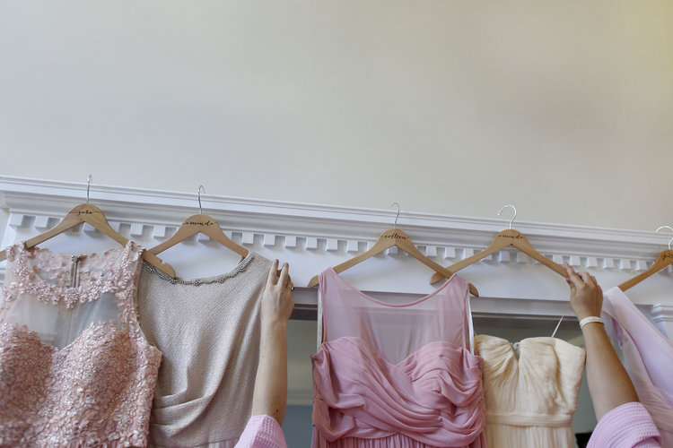 Arms of women reaching for formal dresses hanging from white molding