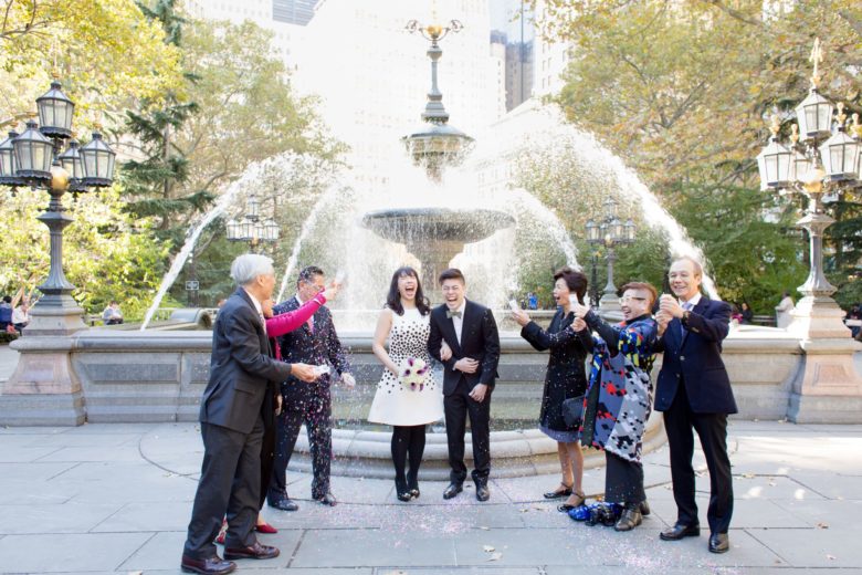 Couple, with their families, being showered in confetti in front of a fountain