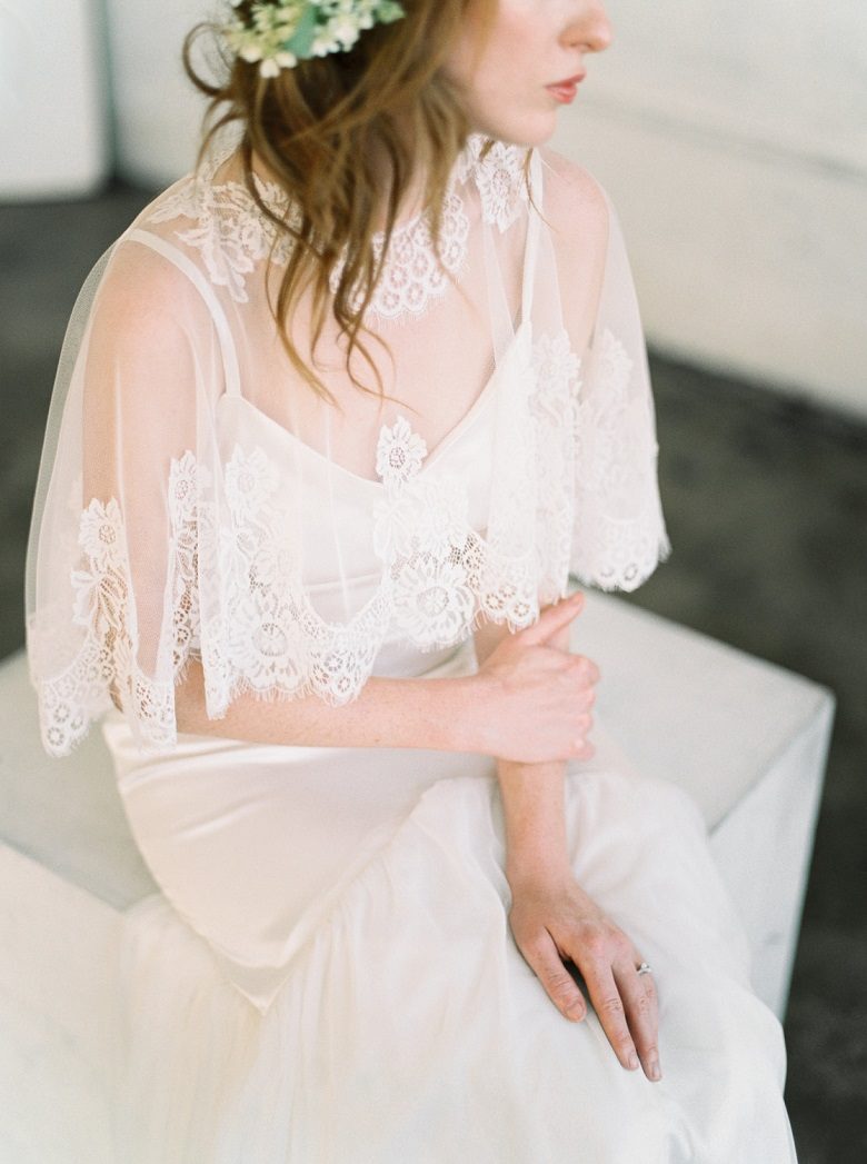 A bride sits wearing her lightweight wedding dress with a lace capulet