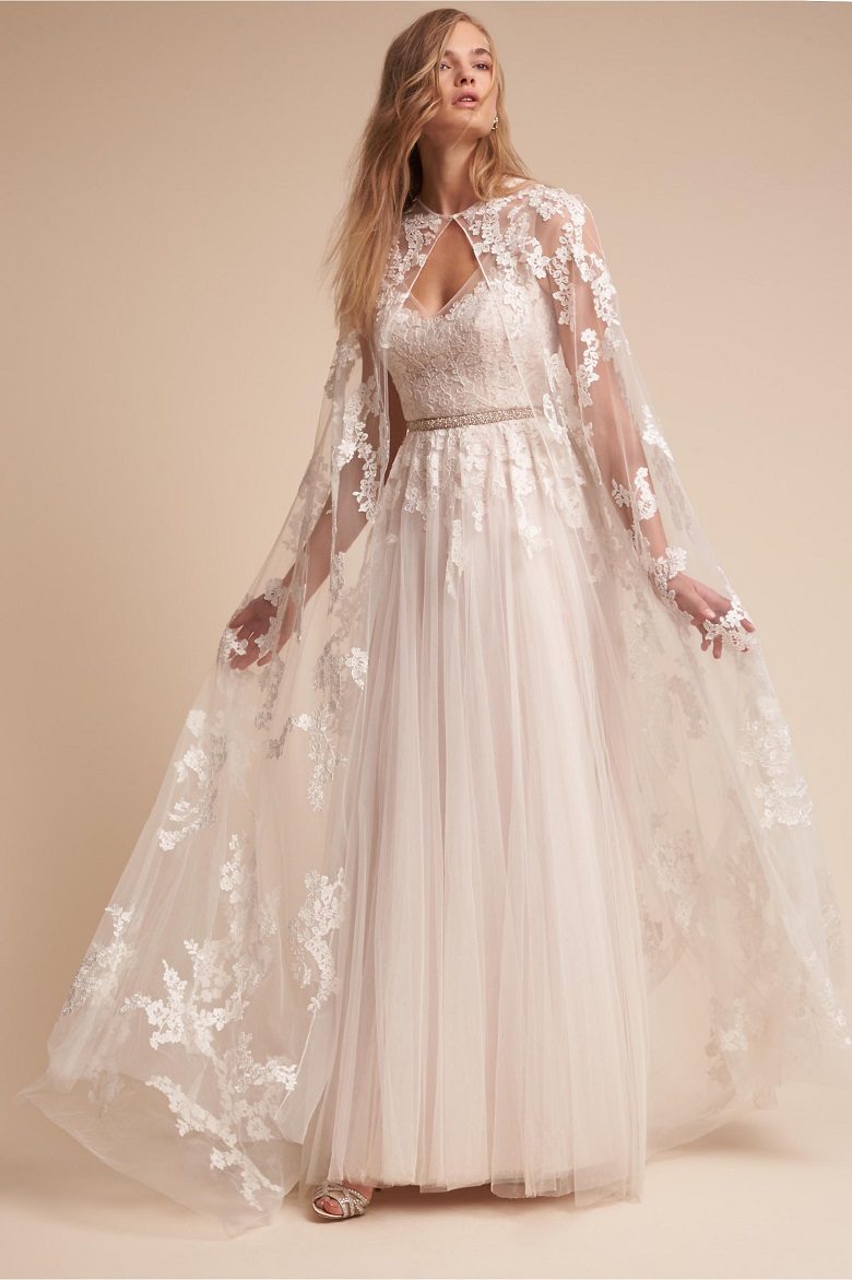 A bride with a lightweight, long wedding dress and a lace full length cape