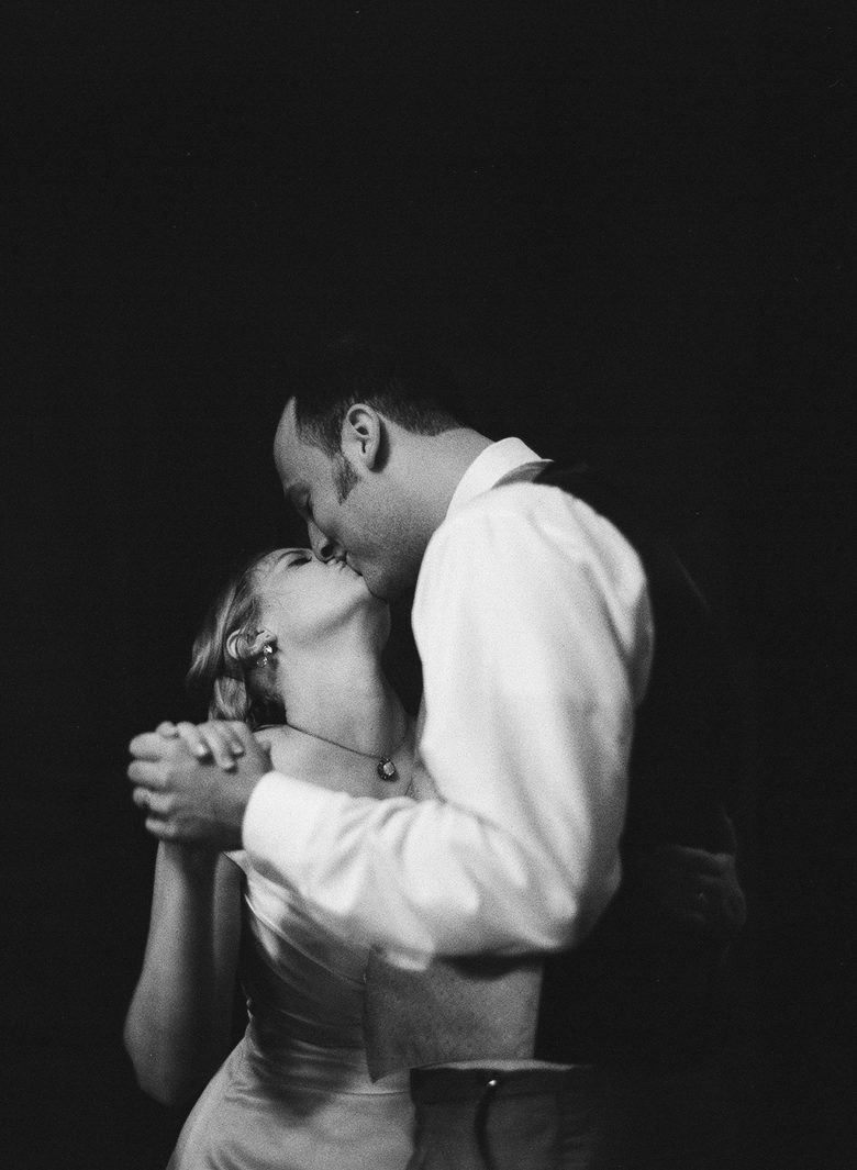 bride and groom kissing while dancing, in black and white