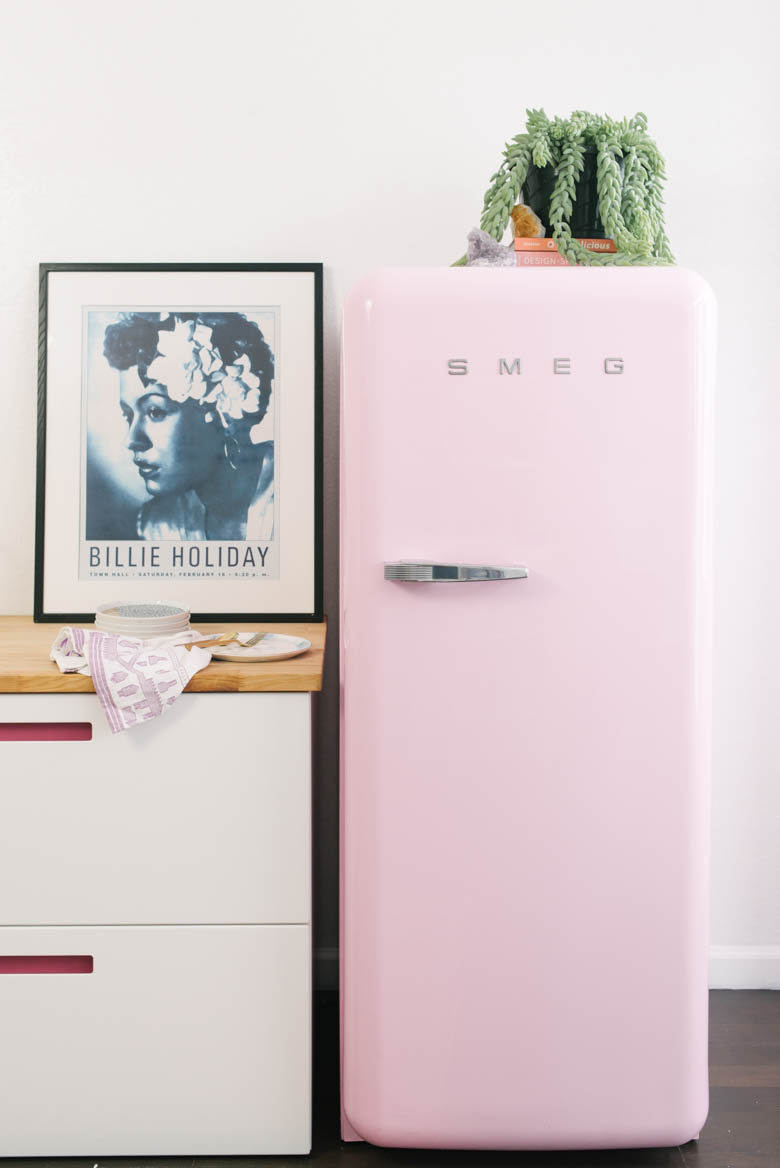 Pink Smeg Fridge next to wooden countertop with Billie Holiday poster and succulent