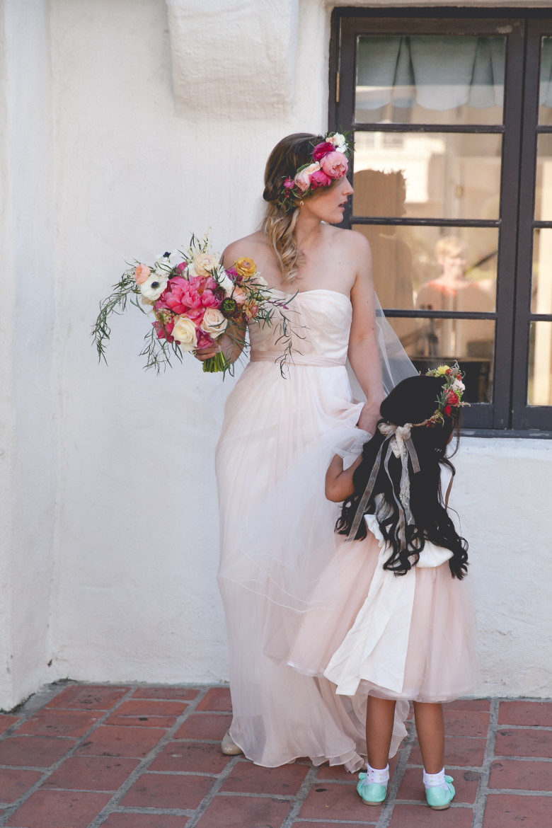 a bride holds her bouquet in one hand while looking to her left, as her flower girl clings to her 