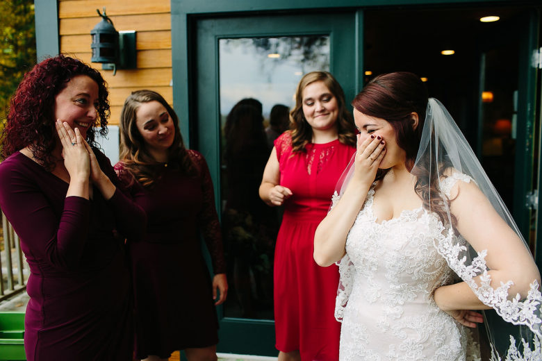 Bride laughing, covering mouth, with three girlfriends in front of green door