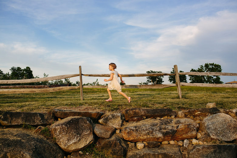 young girl in white dress frolicking in a field with a wooden fence