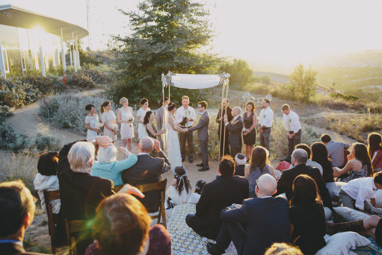 A Jewish wedding ceremony taking place on a hillside as the sun is setting