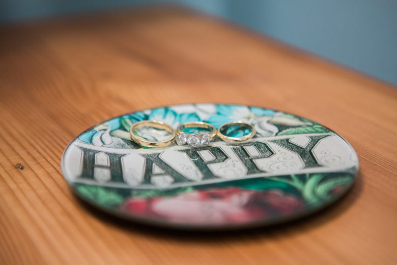 Small round plate with the word "happy" written across it with three wedding rings on it.