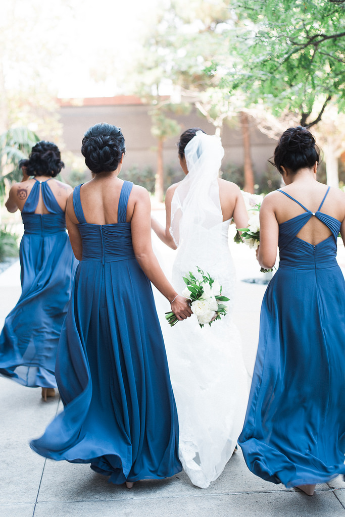 A bride and her wedding party walk away with their backs towards the camera.