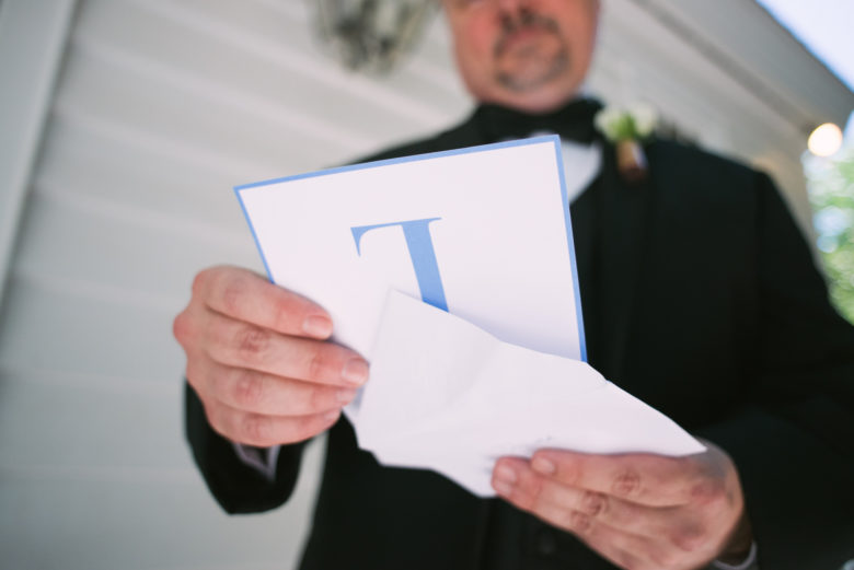Man in tux holds envelope and card with large blue L 