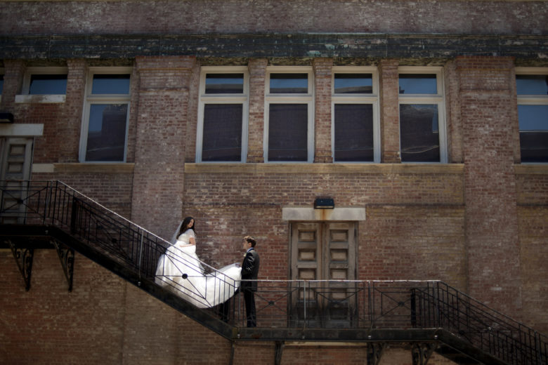 groom holding brides train on fire escape as she looks back at him