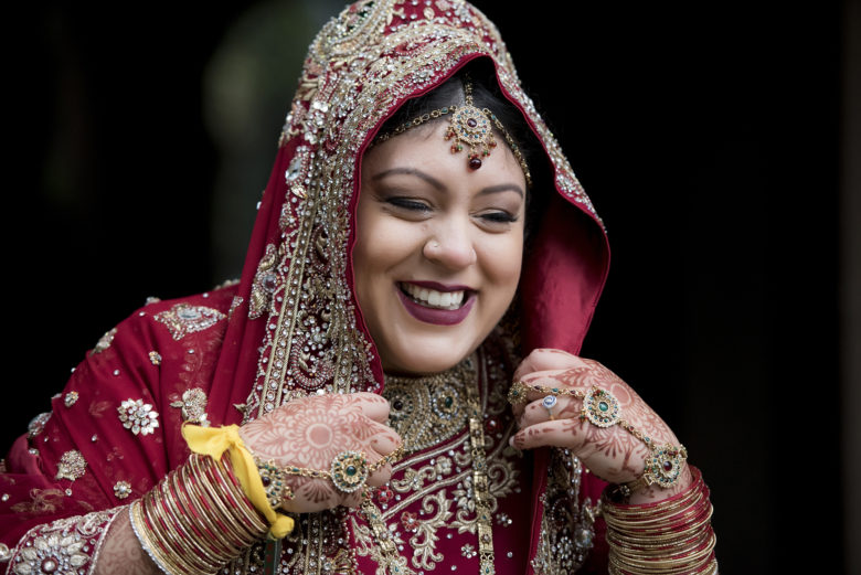 bejeweled bride wearing ornately embellished red attire with henna and bangles