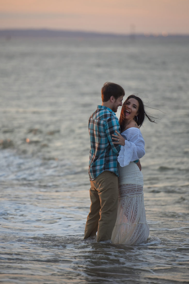 couple fully clothed standing knee-deep in water at sunset, laughing
