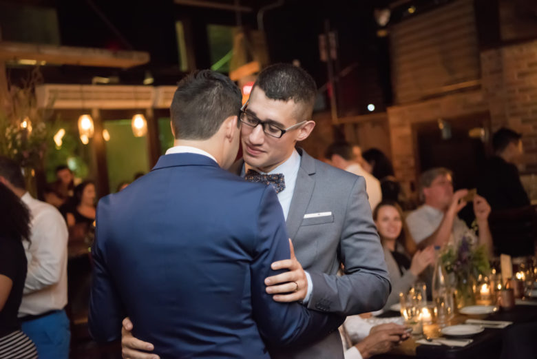 two grooms embracing at candle-lit reception