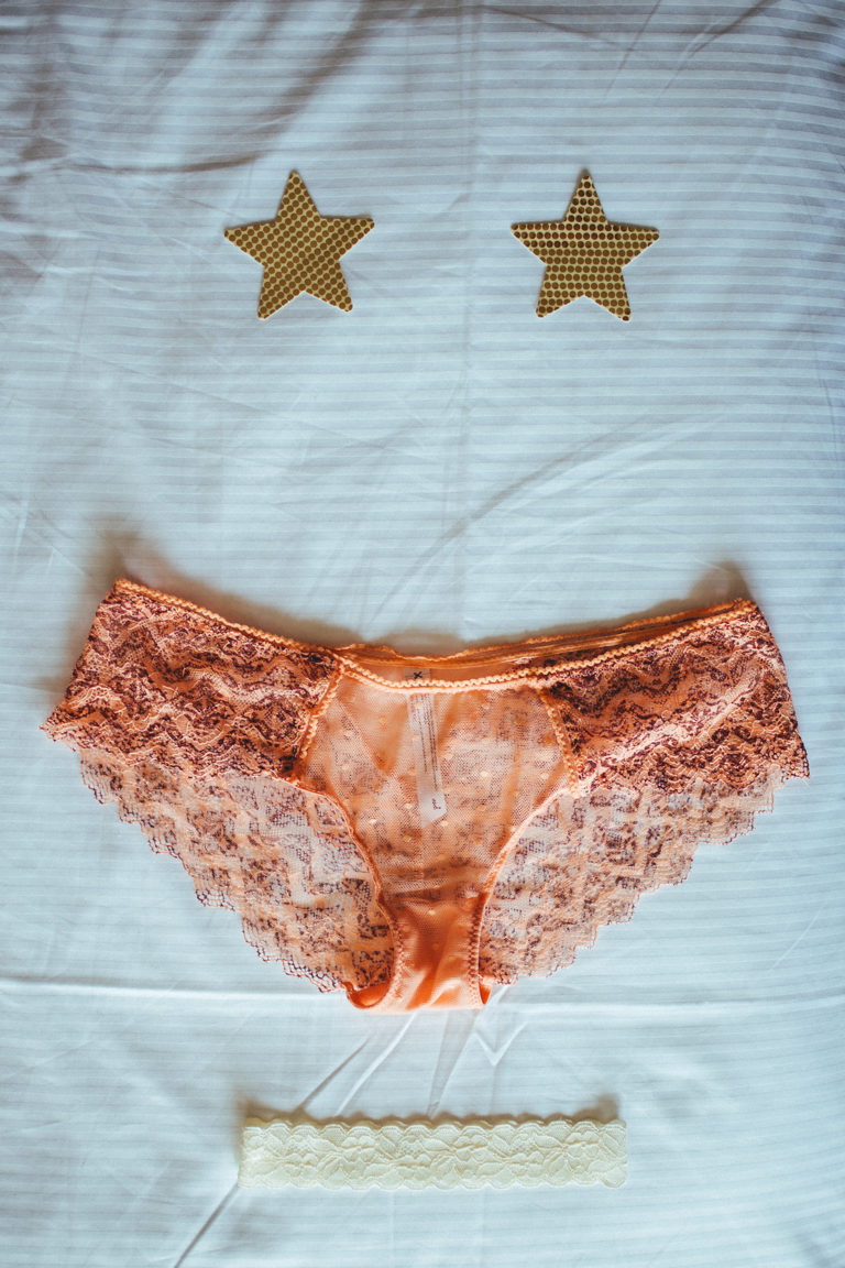 Star pasties, lacy lingerie, and a garter arranged on a bedspread