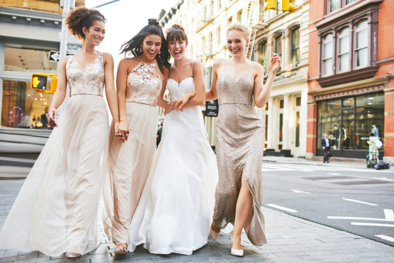 Bride and bridesmaids walking together on city streets.