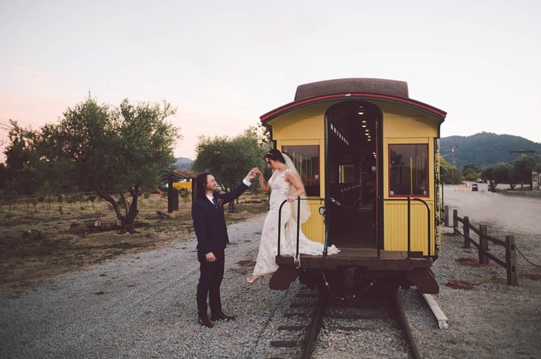 A woman in a wedding gown disembarking a train while holding hands with a man in a dark suit