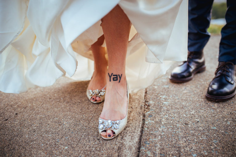 bride's feet in open-toed bejeweled ivory shoes with a Yay ankle tattoo