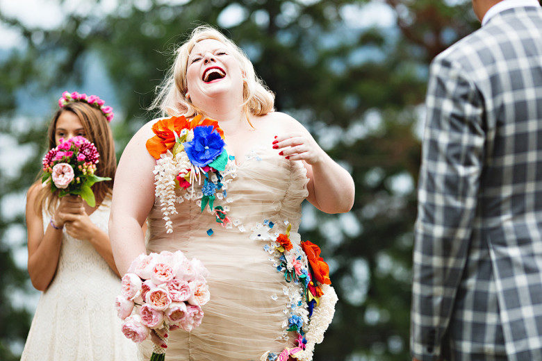 bride in a rouched ivory dress emblazoned with brightly colored flowers with her head back, laughing