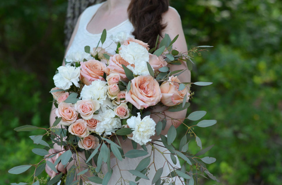 bride holiding bouquet of peach roses and white carnations and eucalyptus