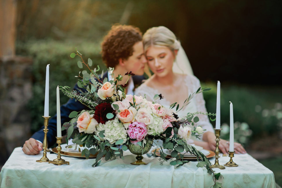 couple at sweetheart table behind centerpiece of heirloom roses and eucalyptus