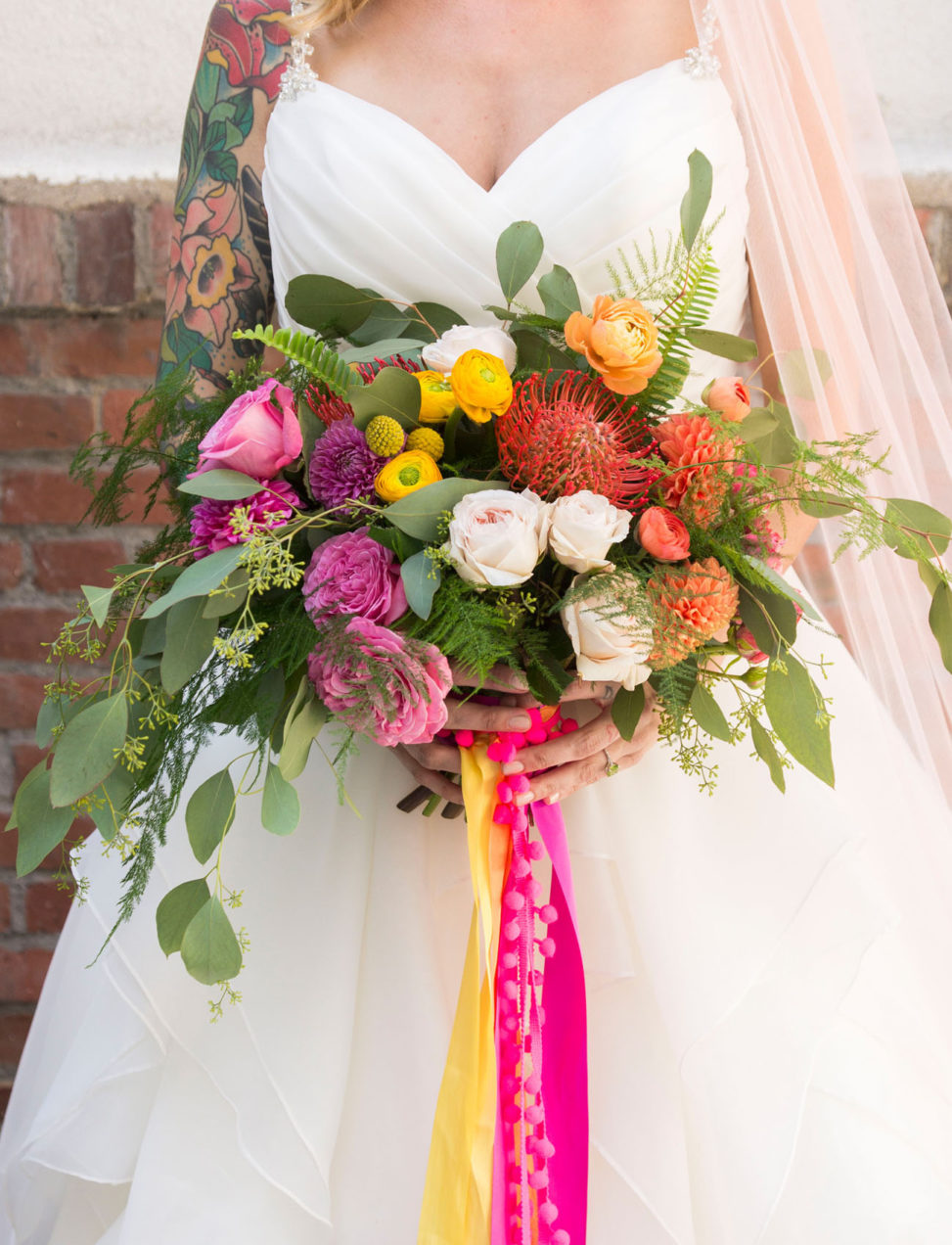 tattooed bride holding brightly colored bouquet with pink and yellow ribbons