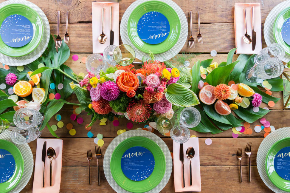 wooden table set with green and blue place settings and pink and yellow centerpieces