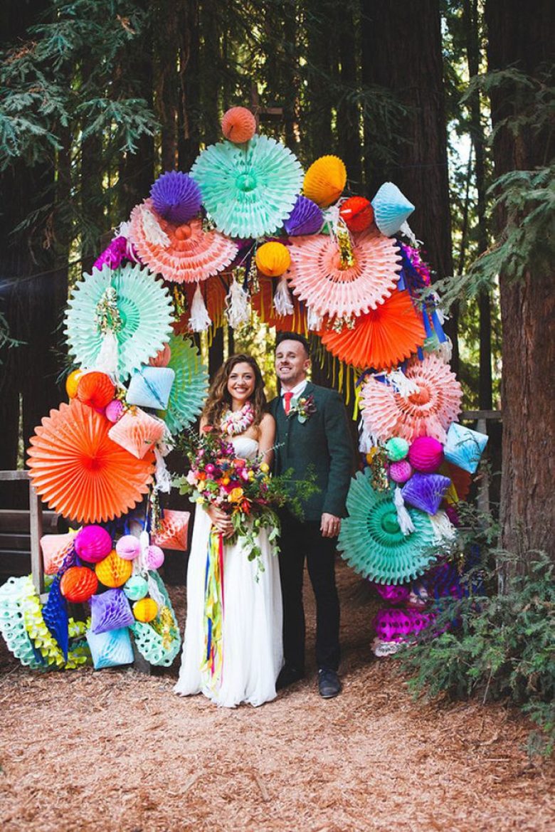 wouple stands beneath an arch made of colorful paper pinwheels and honeycomb decorations