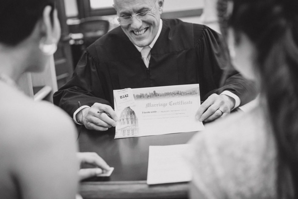 Two women sitting in front of a clerk being presented their marriage license