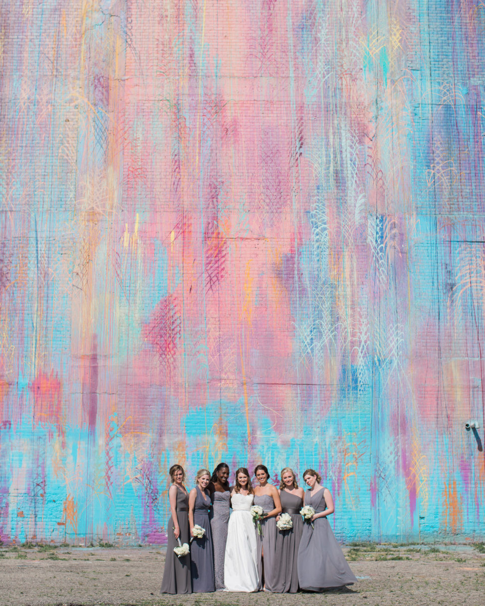 a bride and her bridal party stand together with a large abstract mural backdrop