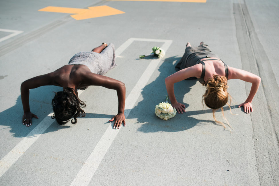 a bride and bridesmaid doing pushups in a parking lot
