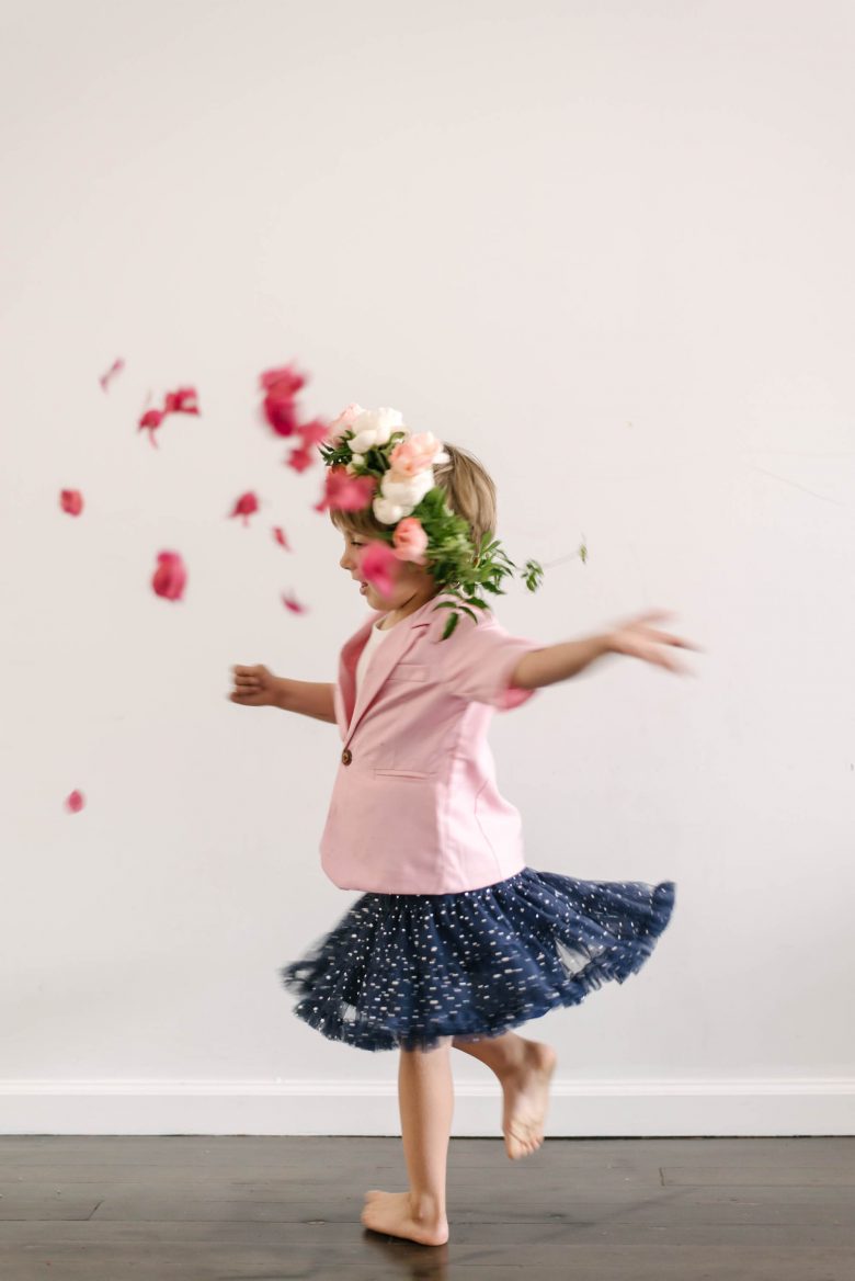 a young boy wearing a pink blazer and navy tutu throws flower petals
