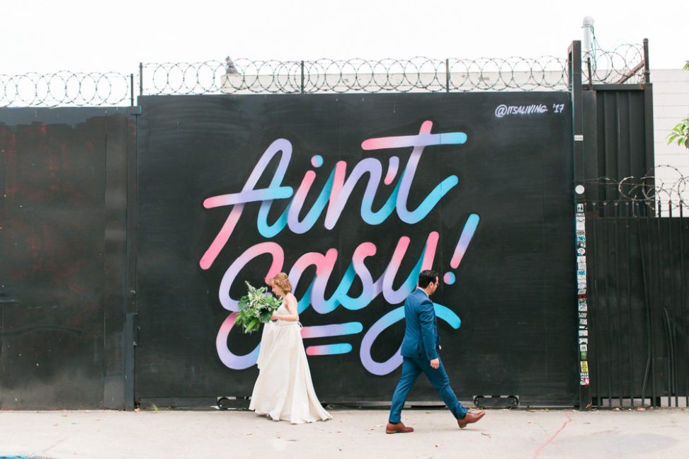 couple in wedding dress and suit in front of mural that says ain't easy