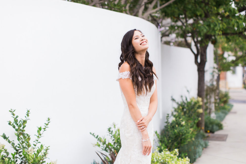 a bride stands against a while wall, smiling