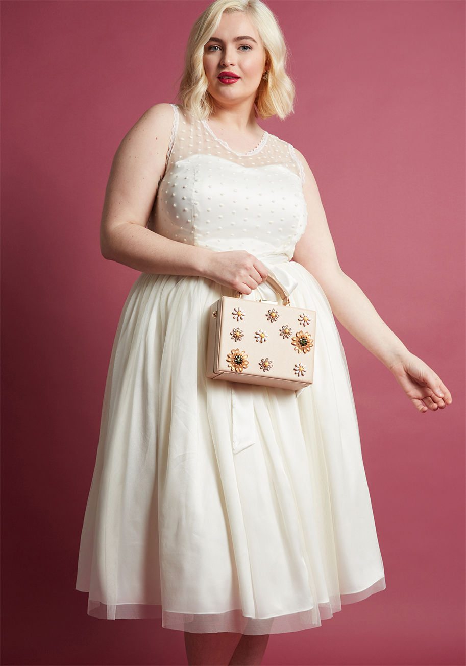 Plus size woman wearing a white, high-neck, knee length dress holding an embellished purse