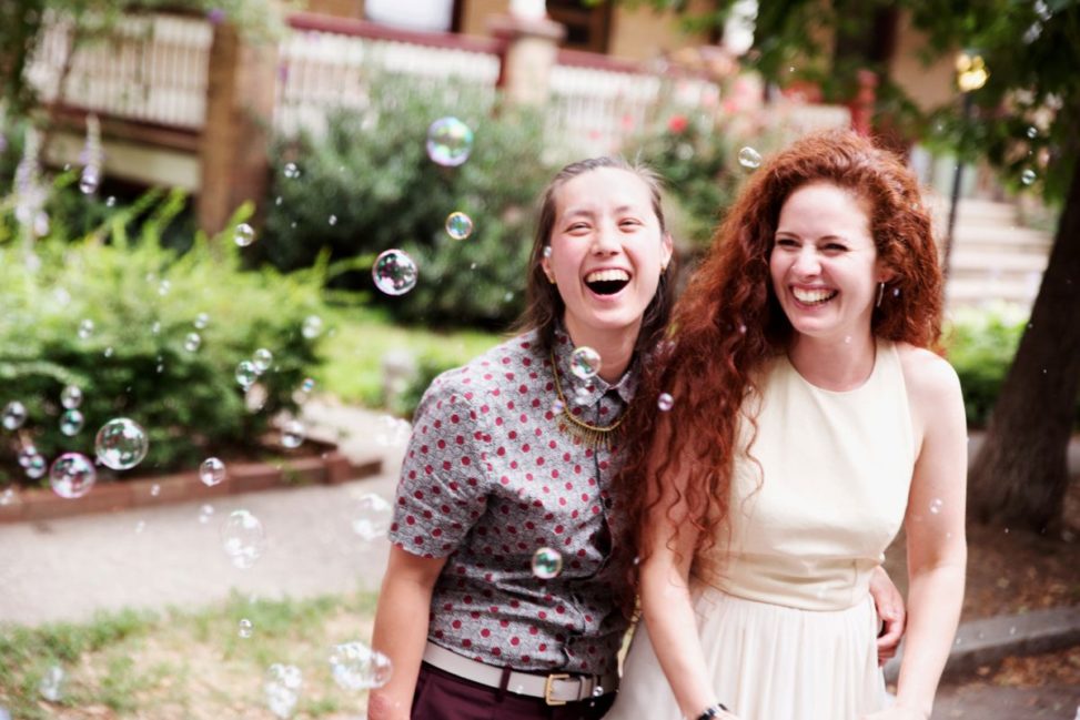 two women smile and laugh while bombarded with bubbles