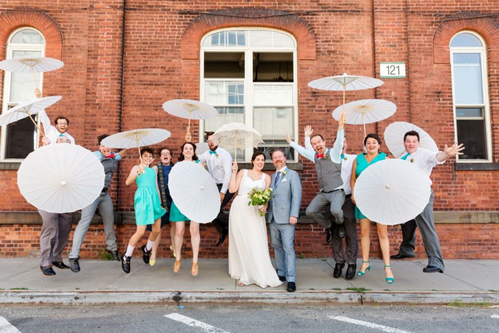 a wedding party jumps in the air with umbrellas