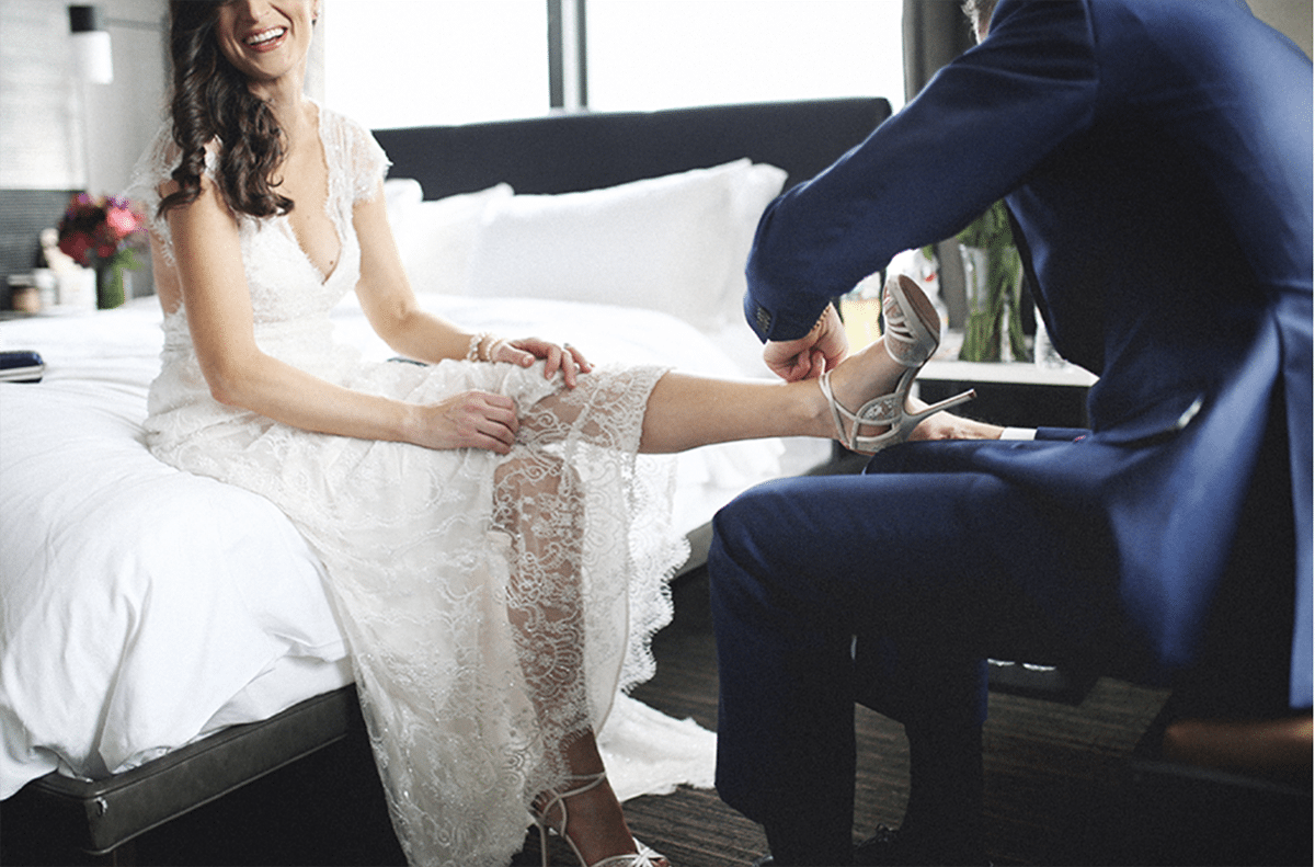 a man helps a bride with her high heels on an urban hotel bed