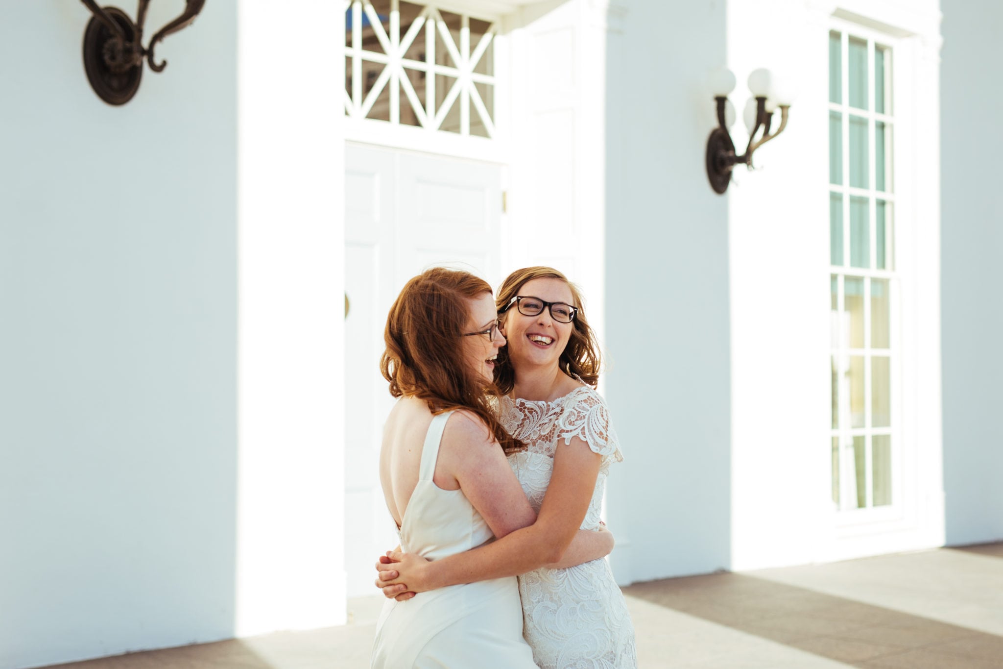 two women in white dresses hug and smile and hug and smile
